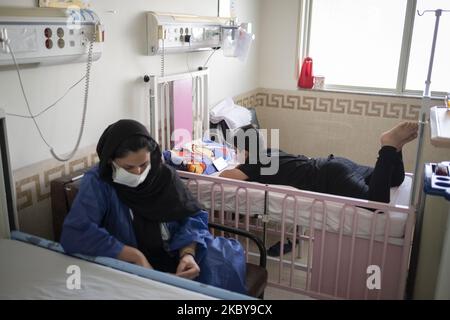 Der 8,5-jährige iranische Junge Mahan, der von der neuen Coronavirus-Krankheit infiziert ist, nutzt sein Smartphone, als seine Mutter Sara (L) mit einer schützenden Gesichtsmaske am 6. September 2020 neben seinem Krankenhausbett im COVID-19-Abschnitt des Ali Asghar Kinderkrankenhauses im Norden Teherans sitzt. Die Iraner dachten, dass Kinder sich nicht mit dem COVID-19 infizieren würden, aber sie erkannten, dass Kinder jeden Alters mit der neuen Coronavirus-Krankheit infiziert werden, aber die meisten von ihnen, die infiziert sind, werden nicht so krank wie Erwachsene. (Foto von Morteza Nikoubazl/NurPhoto) Stockfoto