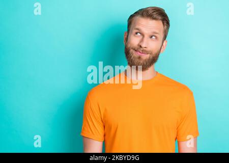 Porträt von fröhlich gut aussehend nachdenklich Kerl mit blondem Bart tragen orange T-Shirt suchen leeren Raum isoliert auf blauem Hintergrund Stockfoto