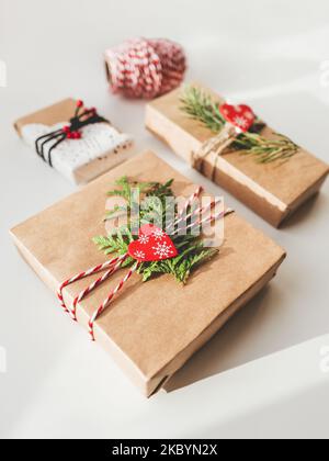 Weihnachten DIY Geschenke verpackt in Bastelpapier mit Tannenzweigen und roten Herzen. Dekorationen für Neujahrsgeschenke. Festlicher Hintergrund. Winterurlaub Stockfoto