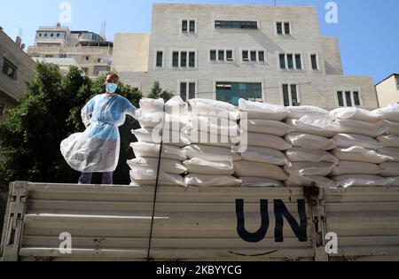 Ein Mitarbeiter des Hilfswerks der Vereinten Nationen für Palästina-Flüchtlinge (UNRWA), der aufgrund der COVID-19-Coronavirus-Pandemie in Maske und Schutzkleidung gekleidet ist, steht am 15. September 2020 auf einem Lastwagen, der in Gaza-Stadt Nahrungsmittelhilfe für bedürftige Familien bereitstellt. (Foto von Majdi Fathi/NurPhoto) Stockfoto