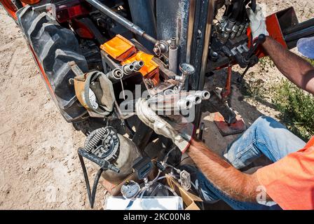 Ein männlicher Arbeiter, der Handschuhe trägt, arbeitet mit Gewinderohren, während er auf einem Traktor in einer aktiven Deponie arbeitet. Stockfoto