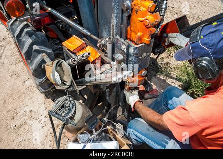 Ein männlicher Arbeiter, der Handschuhe und Gehörschutz trägt, arbeitet mit Gewinderohren, während er auf einem Traktor auf einer aktiven Deponie unterwegs ist. Stockfoto