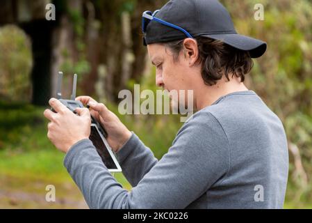 Ein junger hispanischer Mann in einer Kappe, der tagsüber eine Drohne auf einem Feld betreibt Stockfoto