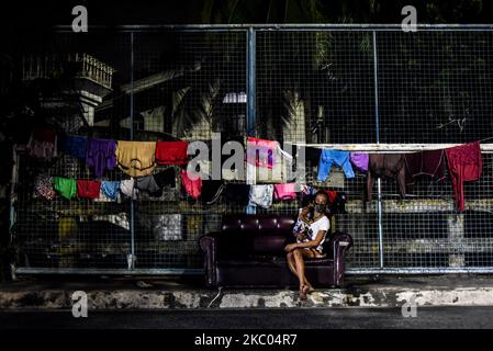 Eine Frau, die eine Gesichtsmaske trägt, trägt ihre Tochter, während sie am 18. September 2020 auf einem Sofa entlang einer Straße in Quezon City, Philippinen, sitzt. (Foto: Lisa Marie David/NurPhoto) Stockfoto