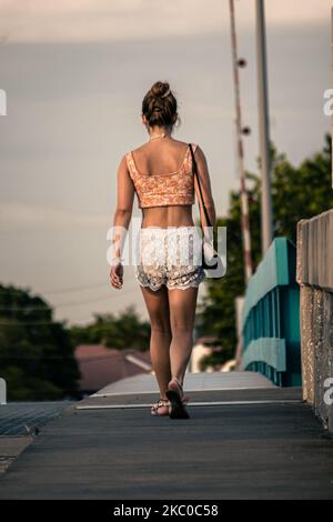 Die junge Frau im Sommeroutfit geht auf der Straße, Rückseite, vertikal Stockfoto