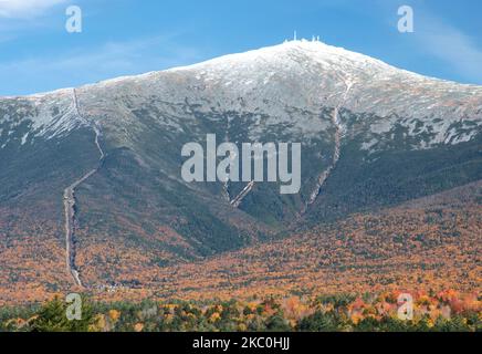 Blauer Himmel und farbenprächtiges Herbstlaub mit Schnee auf dem Mount Washington in New Hampshire. Links sind Spuren von Zahnradbahn und Antenne auf dem Gipfel zu sehen. Stockfoto