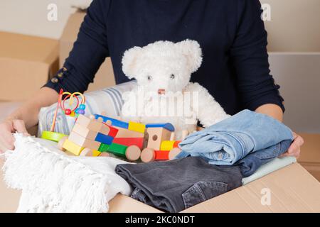 Spenden, Wohltätigkeit, Hilfe für Familien mit niedrigem Einkommen Konzept. Frau sammelt ehrenamtlich Spendenbox mit Kleidung, Bettwäsche, Kinderspielzeug Stockfoto