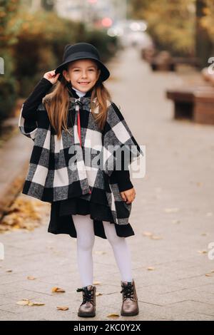 Ein stilvolles kleines Mädchen im Hut geht durch die Herbststadt Stockfoto