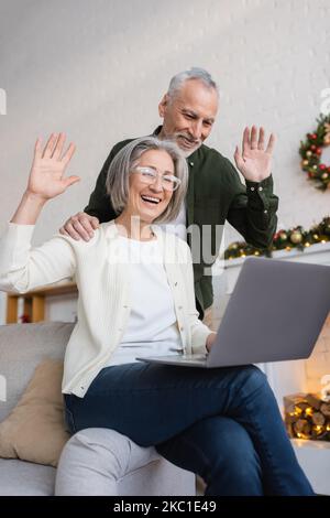 Glücklicher Mann und Frau mittleren Alters winken während eines Videoanrufs an den weihnachtsfeiertagen die Hände Stockfoto