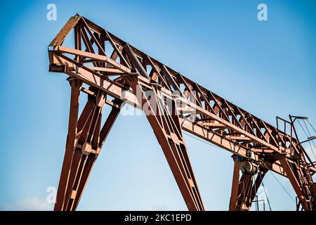 Alter rostiger Portalkran auf verlassene Baustelle. Baumaschinen gegen blauen Himmel. Metallausrüstung in Fabriken, Industrie. Stockfoto