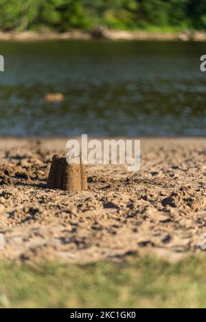 Eine vertikale Aufnahme einer kleinen Sandburg, die am Ufer eines Flusses isoliert ist Stockfoto