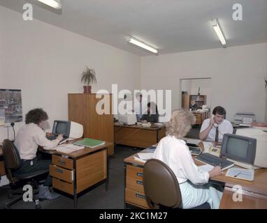 1989, historisches, männliches und weibliches Personal in einem offenen Büro, das an Holztischen sitzt und mit den kleinen Computerterminals der Zeit arbeitet, England, Großbritannien. Stockfoto