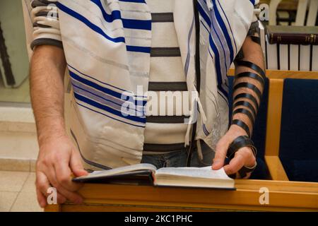 Ein erwachsener jüdischer Mann, der mit einem Tefillin auf seinem Arm betet, ein bibelbuch hält, während er ein Gebet bei einem jüdischen Ritual liest Stockfoto