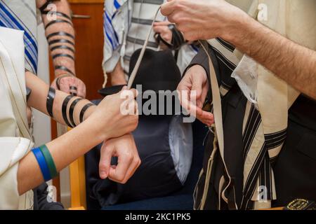 Ein orthodoxer Mann, der ein Gebetstuch trug, legte im Rahmen einer jüdischen Zeremonie, Bar Mitzvah, einem jungen Mann einen jüdischen Tefillin auf den Arm, der sich auf ein Gebet vorbereitete Stockfoto