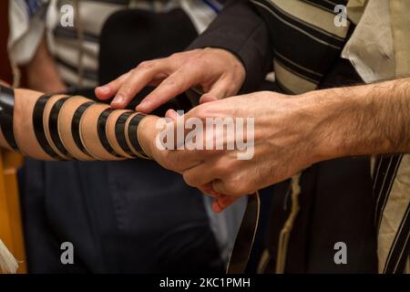 Ein orthodoxer Mann, der ein Gebetstuch trug, legte im Rahmen einer jüdischen Zeremonie, Bar Mitzvah, einem jungen Mann einen jüdischen Tefillin auf den Arm, der sich auf ein Gebet vorbereitete Stockfoto