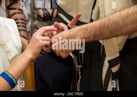 Ein orthodoxer Mann, der ein Gebetstuch trug, legte im Rahmen einer jüdischen Zeremonie, Bar Mitzvah, einem jungen Mann einen jüdischen Tefillin auf den Arm, der sich auf ein Gebet vorbereitete Stockfoto