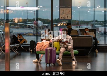 Passagiere mit Gesichtsmaske sitzen vor dem Fenster und das Flugzeug im Hintergrund. Passagiere mit Gesichtsmasken, Gesichtsschutz, Handschuhen und anderen Sicherheitsmaßnahmen sind im Flughafenterminal zu sehen. Im Bereich F Gates des Internationalen Flughafens Wien VIE LOWW - Flughafen Wien-Schwechat, der die österreichische Hauptstadt, aber auch Bratislava bedient, da es während der Covid-19 Coronavirus-Pandemie 55km von der slowakischen Stadt entfernt ist. Es kommt eine zweite Welle, während die Fälle zunehmen, Gesichtsmask obligatorisch wird, soziale Distanzierungsmaßnahmen und desinfizierende Händedesinfektionsmittel überall sind, während neue Sperren Stockfoto