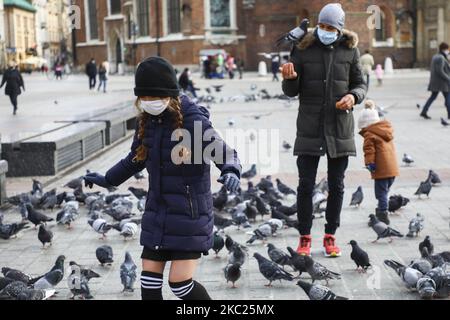 Touristen tragen Gesichtsmasken, während sie während der Coronavirus-Pandemie am Hauptplatz Tauben füttern. Krakau, Polen, am 18.. Oktober 2020. Aufgrund der zunehmenden Verbreitung von COVID-19 in Polen wird das gesamte Gebiet des Landes als „gelbe“ Zone ausgewiesen, und 152 Grafschaften und Städte, einschließlich Krakau, werden ab Oktober 17 als rot markiert. (Foto von Beata Zawrzel/NurPhoto) Stockfoto