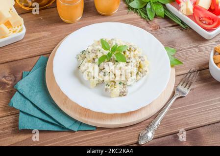 Gekochter Kartoffelsalat mit gekochtem Rindfleisch und Eiern, gewürzt mit Mayonnaise auf einem weißen Teller auf dunklem Holzboden. Stockfoto