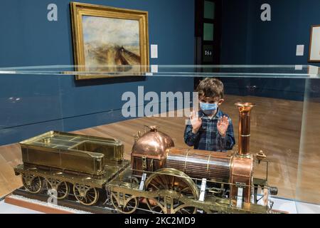 (NUR FÜR REDAKTIONELLE ZWECKE) Ein Junge sieht sich das Dampflokomotive-Modell an, das neben „Rain, Steam and Speed – The Great Western Railway“, 1844, von JMW Turner (1775-1851), während einer Fotoausstellung zur Eröffnung der Ausstellung „Turner's Modern World“ in der Tate Britain (28. Oktober 2020 - 7. März 2021) gezeigt wird. Am 26. Oktober 2020 in London, England, dem größten britischen Landschaftsmaler gewidmet. (Foto von Wiktor Szymanowicz/NurPhoto) Stockfoto