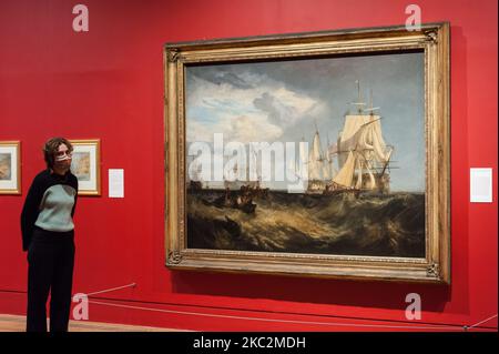 (NUR ZUR REDAKTIONELLEN VERWENDUNG) Ein Mitarbeiter der Galerie posiert neben „Spithead: Two Captured Danish Ships Entering Portsmouth Harbour“, 1807–9 von JMW Turner (1775-1851) während einer Fotoausstellung zur Eröffnung der Ausstellung „Turner's Modern World“ in der Tate Britain (28. Oktober 2020 - 7. März 2021), die dem größten britischen Landschaftsmaler gewidmet ist, am 26. Oktober 2020 in London, England. (Foto von Wiktor Szymanowicz/NurPhoto) Stockfoto