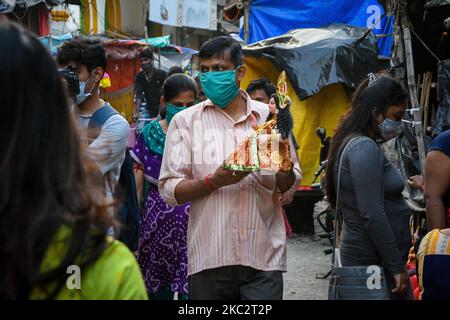 Ein Gentleman mit Maske nimmt vor der Festfeier in Kalkutta, Indien, am 28. Oktober 2020 ein Idol von Devi Lakshmi mit nach Hause. Lakshmi puja ist das Fest der verehrenden Göttin Lakshmi, der hinduistischen Göttin des Reichtums und Wohlstands. Es wird am Vollmondtag nach Durga Dashami (dem letzten Tag von Durga puja) gefeiert. Anhänger glauben, dass am Tag der Lakshmi puja , die Göttin besucht ihre Anhänger nach Hause , bringt mit ihrem guten Reichtum und Wohlstand für die Familie. Die Frau der Familie verehrt die Göttin Lakshmi am Tag, nachdem sie ihr Haus gereinigt und Alpona auf den Boden gezeichnet hat Stockfoto