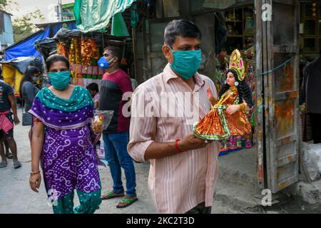 Ein Gentleman mit Maske nimmt vor der Festfeier in Kalkutta, Indien, am 28. Oktober 2020 ein Idol von Devi Lakshmi mit nach Hause. Lakshmi puja ist das Fest der verehrenden Göttin Lakshmi, der hinduistischen Göttin des Reichtums und Wohlstands. Es wird am Vollmondtag nach Durga Dashami (dem letzten Tag von Durga puja) gefeiert. Anhänger glauben, dass am Tag der Lakshmi puja , die Göttin besucht ihre Anhänger nach Hause , bringt mit ihrem guten Reichtum und Wohlstand für die Familie. Die Frau der Familie verehrt die Göttin Lakshmi am Tag, nachdem sie ihr Haus gereinigt und Alpona auf den Boden gezeichnet hat Stockfoto