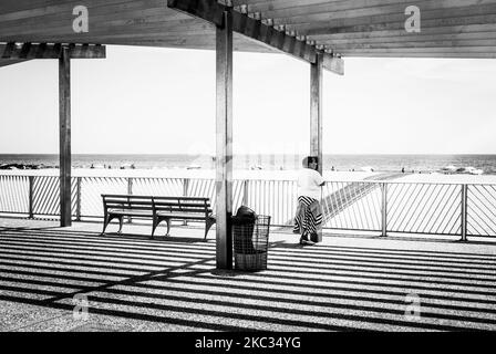 Eine Graustufenaufnahme einer Frau, die auf einer Strandpromenade im Schatten steht Stockfoto