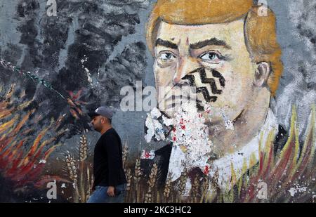 Ein Palästinenser geht an Graffiti vorbei, das den scheidenden US-Präsidenten Donald Trump zeigt, mit einem Fußabdruck auf seinem Gesicht, der am 8. November 2020 an einer Wand entlang einer Straße in Gaza-Stadt gezeichnet wurde. (Foto von Majdi Fathi/NurPhoto) Stockfoto