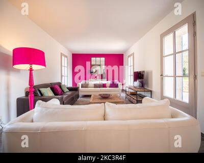 Ein kleines, modernes und helles Wohnzimmer mit zwei weißen Sofas, einem braunen Sofa und einer rosa Lampe Stockfoto