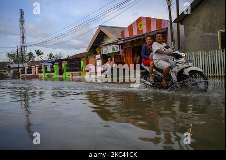 Motorradfahrer überqueren am 14. November 2020 eine Pfütze, die aufgrund von Überschwemmungen in Lere Village, Palu, Provinz Central Sulawesi, Indonesien, eine Straße blockiert. Die Überschwemmungen, die fünf Tage im Monat andauern, werden nicht nur durch hohe Gezeiten verursacht, sondern auch durch eine bis zu 1,5 Meter tiefe Landsenkung aufgrund des Erdbebens der Stärke 7,4 vor zwei Jahren an der Küste von Palu Bay. Das Erdbeben, das den Tsunami und die Verflüssigung auslöste, tötete mehr als 5.000 Einwohner. (Foto von Basri Marzuki/NurPhoto) Stockfoto