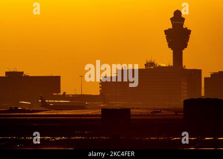 Goldene Stunde bei Sonnenaufgang und Sonnenaufgang mit warmen Himmelsfarben der magischen Stunde am internationalen Flughafen Amsterdam Schiphol AMS EHAM in den Niederlanden. Frühmorgendliche Aufnahmen der Luftfahrtindustrie mit der Silhouette des Kontrollturms und des Landeflugzeugs im bunten europäischen Skyscape. 22. November 2020 (Foto von Nicolas Economou/NurPhoto) Stockfoto