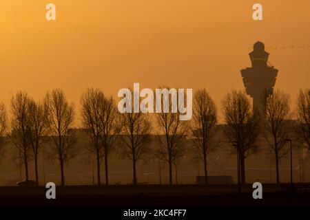 Goldene Stunde bei Sonnenaufgang und Sonnenaufgang mit warmen Himmelsfarben der magischen Stunde am internationalen Flughafen Amsterdam Schiphol AMS EHAM in den Niederlanden. Frühmorgendliche Aufnahmen der Luftfahrtindustrie mit der Silhouette des Kontrollturms und des Landeflugzeugs im bunten europäischen Skyscape. 22. November 2020 (Foto von Nicolas Economou/NurPhoto) Stockfoto