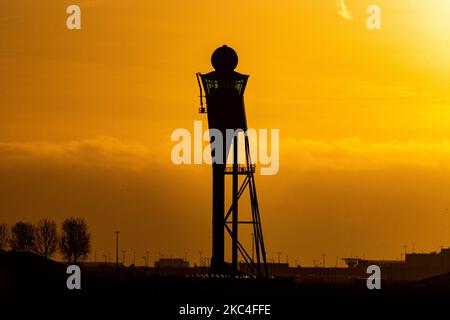 Goldene Stunde bei Sonnenaufgang und Sonnenaufgang mit warmen Himmelsfarben der magischen Stunde am internationalen Flughafen Amsterdam Schiphol AMS EHAM in den Niederlanden. Frühmorgendliche Aufnahmen der Luftfahrtindustrie mit der Silhouette des Kontrollturms und des Landeflugzeugs im bunten europäischen Skyscape. 22. November 2020 (Foto von Nicolas Economou/NurPhoto) Stockfoto