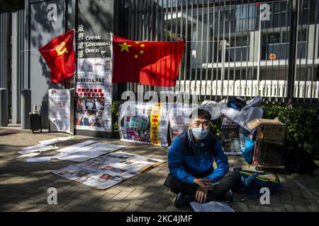 Prodemokratische Demonstranten werden beim Lesen einer Zeitung vor der Flagge der Kommunistischen Partei und der chinesischen Flagge vor dem Zentralregierungsbüro vor dem Zeitpunkt gesehen, als Carrie Lam am am 25. November 2020 in Hongkong, China, die politische Ansprache im Legislativrat halten wird. Die Hongkonger Chefin Carrie Lam hält heute nach wenigen Wochen Verspätung ihre Rede zur Politik. (Foto von Vernon Yuen/NurPhoto) Stockfoto