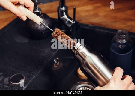 Waschen Reinigung wiederverwendbare Trinkflasche mit Kokosfaser-Fläschchenreinigungsbürste in der heimischen Küche. Nachhaltiges Lifestyle-Konzept. Stockfoto