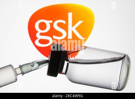 Eine medizinische Spritze und ein Fläschchen vor dem Logo des Pharmaunternehmens GlaxoSmithKline (GSK) sind auf diesem kreativen illustrativen Foto zu sehen. Weltweit sind mehr als hundertfünfzig COVID-19-Coronavirus-Impfstoffe in der Entwicklung, von denen mehrere die dritte Phase klinischem Studien aufweisen, wie Medien berichteten. (Foto-Illustration von STR/NurPhoto) Stockfoto