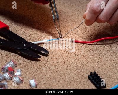 Löten - Verbindungsdrähte mit Zinn und Lötkolben, Werkstatt, im Hintergrund elektrische Elemente, Kabel Stockfoto