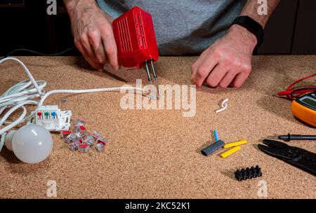 Löten - Verbindungsdrähte mit Zinn und Lötkolben, Werkstatt, im Hintergrund elektrische Elemente, Kabel Stockfoto