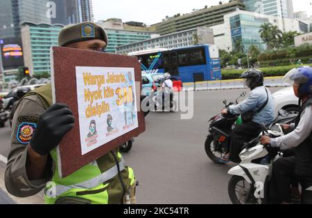 Beamte der Polizeieinheit des öffentlichen Dienstes der Provinz Jakarta (Satpol PP) zeigen Autofahrern, die am 30. November 2020 Jalan MH Thamrin, Menteng, Jakarta überqueren, Plakate mit der Präventionskampagne Covid-19. Die Zahl der Covid-19-Verbreitung in Jakarta ist noch nicht zurückgegangen, die DKI-Regierung der Provinz Jakarta bemüht sich weiterhin, die Ausbreitung zu verhindern, indem sie die Bewohner daran erinnert, Distanz zu bewahren, sich die Hände zu waschen und im Freien immer Masken zu verwenden. (Foto von Dasril Roszandi/NurPhoto) Stockfoto