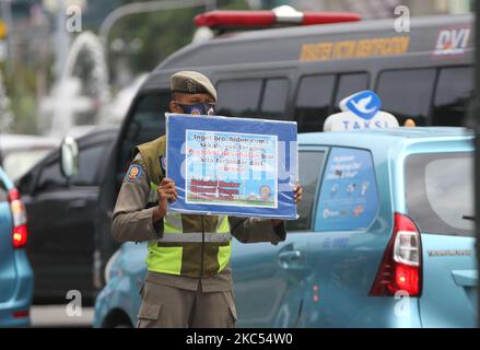 Beamte der Polizeieinheit des öffentlichen Dienstes der Provinz Jakarta (Satpol PP) zeigen Autofahrern, die am 30. November 2020 Jalan MH Thamrin, Menteng, Jakarta überqueren, Plakate mit der Präventionskampagne Covid-19. Die Zahl der Covid-19-Verbreitung in Jakarta ist noch nicht zurückgegangen, die DKI-Regierung der Provinz Jakarta bemüht sich weiterhin, die Ausbreitung zu verhindern, indem sie die Bewohner daran erinnert, Distanz zu bewahren, sich die Hände zu waschen und im Freien immer Masken zu verwenden. (Foto von Dasril Roszandi/NurPhoto) Stockfoto