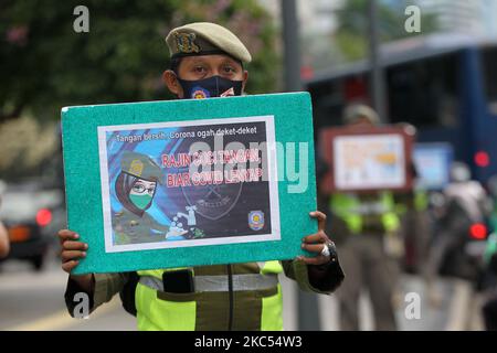 Beamte der Polizeieinheit des öffentlichen Dienstes der Provinz Jakarta (Satpol PP) zeigen Autofahrern, die am 30. November 2020 Jalan MH Thamrin, Menteng, Jakarta überqueren, Plakate mit der Präventionskampagne Covid-19. Die Zahl der Covid-19-Verbreitung in Jakarta ist noch nicht zurückgegangen, die DKI-Regierung der Provinz Jakarta bemüht sich weiterhin, die Ausbreitung zu verhindern, indem sie die Bewohner daran erinnert, Distanz zu bewahren, sich die Hände zu waschen und im Freien immer Masken zu verwenden. (Foto von Dasril Roszandi/NurPhoto) Stockfoto