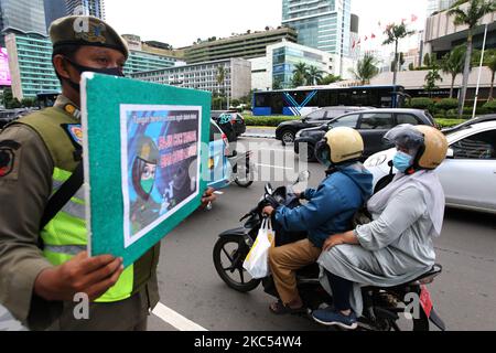 Beamte der Polizeieinheit des öffentlichen Dienstes der Provinz Jakarta (Satpol PP) zeigen Autofahrern, die am 30. November 2020 Jalan MH Thamrin, Menteng, Jakarta überqueren, Plakate mit der Präventionskampagne Covid-19. Die Zahl der Covid-19-Verbreitung in Jakarta ist noch nicht zurückgegangen, die DKI-Regierung der Provinz Jakarta bemüht sich weiterhin, die Ausbreitung zu verhindern, indem sie die Bewohner daran erinnert, Distanz zu bewahren, sich die Hände zu waschen und im Freien immer Masken zu verwenden. (Foto von Dasril Roszandi/NurPhoto) Stockfoto