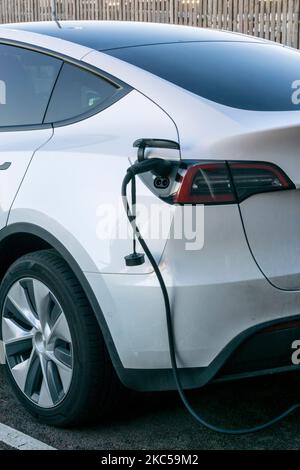 Ein weißes Tesla-Elektroauto, das an einer öffentlichen Ladestation lädt. Stockfoto