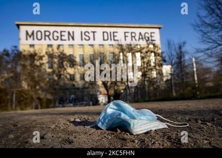 Am 8. Dezember 2020 liegt eine medizinische Maske auf dem Weg zum Eingang des Techno-Clubs Berghain in Berlin. An der Fassade des Gebäudes hängt ein Banner, Kunstwerk des Künstlers Rirkrit Tiravanija, mit der Aufschrift "Morgen ist die Frage". Deutschland, wenn es vor einer Weihnachtssaison mit restriktiven Regeln steht, die private Versammlungen, Handel, Bewegung usw. einschränken, sich von den Bundes- und Kommunalbehörden dazu entschlossen hat, auf die zweite Welle der Coronavirus-Pandemie zu reagieren, da die Anzahl der Fälle nach mehr als einem Monat teilweiser Sperrung, Nimmt ab, aber weit von der gewünschten Schwelle von 50 Fällen für 100,00 Stockfoto