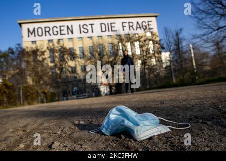 Am 8. Dezember 2020 liegt eine medizinische Maske auf dem Weg zum Eingang des Techno-Clubs Berghain in Berlin. An der Fassade des Gebäudes hängt ein Banner, Kunstwerk des Künstlers Rirkrit Tiravanija, mit der Aufschrift "Morgen ist die Frage". Deutschland, wenn es vor einer Weihnachtssaison mit restriktiven Regeln steht, die private Versammlungen, Handel, Bewegung usw. einschränken, sich von den Bundes- und Kommunalbehörden dazu entschlossen hat, auf die zweite Welle der Coronavirus-Pandemie zu reagieren, da die Anzahl der Fälle nach mehr als einem Monat teilweiser Sperrung, Nimmt ab, aber weit von der gewünschten Schwelle von 50 Fällen für 100,00 Stockfoto