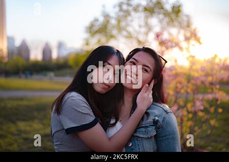 Eine asiatische Mutter und Tochter, die während des Sonnenuntergangs Fotos in einem Garten mit Skyline im Hintergrund machen Stockfoto