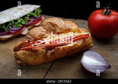 Croissant mit Schinkenkäse und Tomaten auf einem Holzbrett mit Entourage Stockfoto