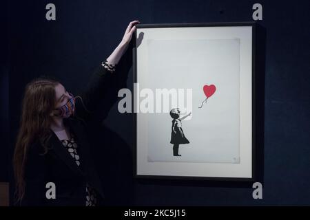 (NUR ZUR REDAKTIONELLEN VERWENDUNG) Ein Mitarbeiter posiert mit Banksy's (geb. 1975) Girl with Balloon, 2004 (est. £120.000 - 180.000) während eines Fotoaufrufs für Bonhams' Prints & Multiples Sale am 10. Dezember 2020 in London, England. (Foto von Wiktor Szymanowicz/NurPhoto) Stockfoto