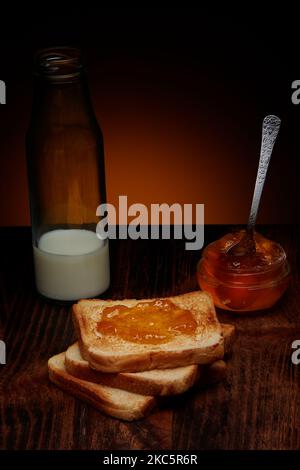 Knusprige Toastscheiben mit Apfelmarmelade und einer Flasche Milch auf einem dunklen Holztisch und einem warmen rustikalen Hintergrund Stockfoto